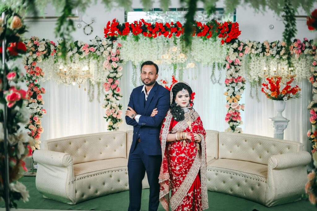 Beautifully adorned Indian couple in traditional attire in a floral-decorated setting.